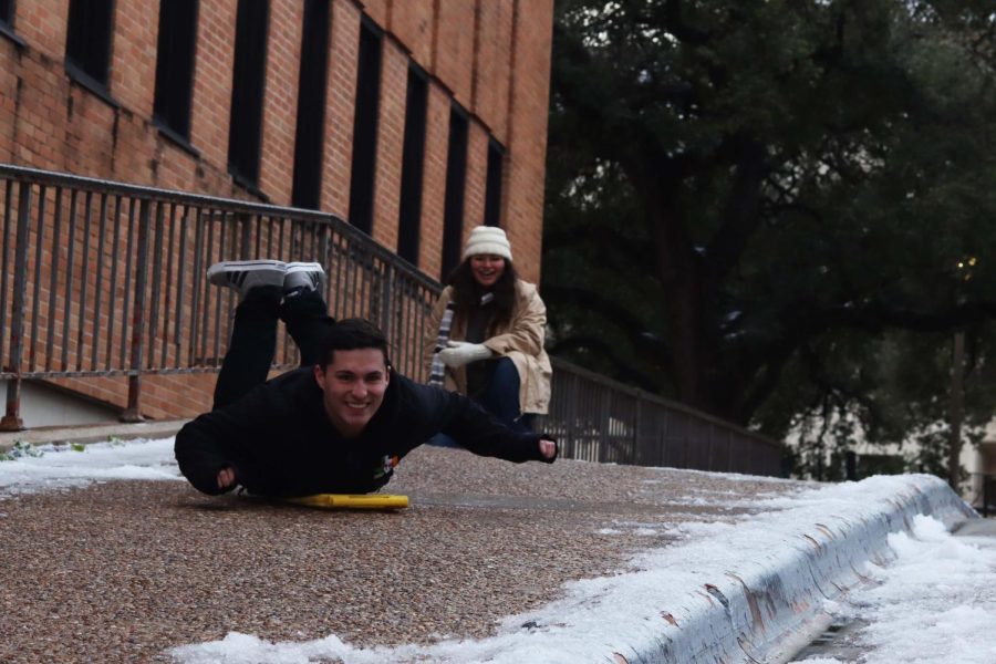 UT student Kennedy Love uses a custodian sign to slide down an icy sidewalk.