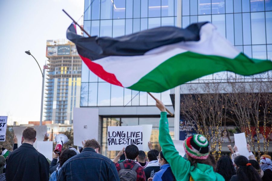 A protester holds a sign reading Long Live Palestine! as a Palestinian flag waves overhead during a protest against the IAC summit on Jan. 21, 2023. 