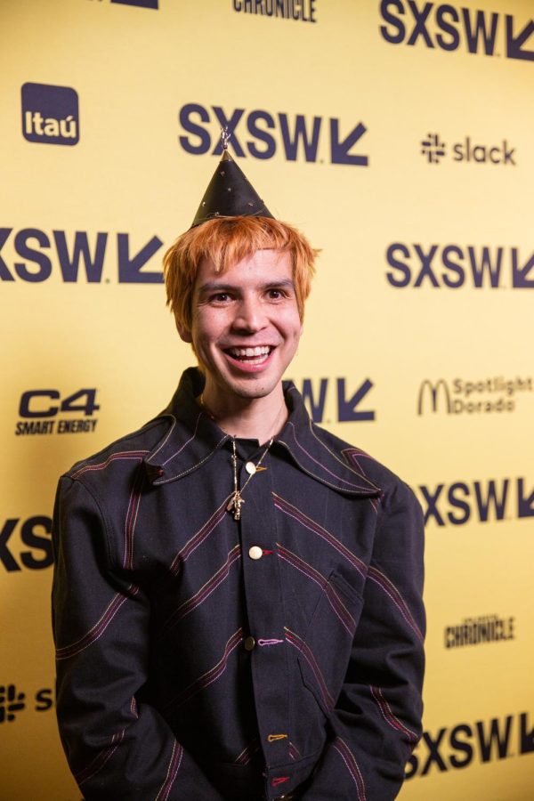 Director Julio Torres, dressed in a striped shirt and a black cone hat, smiles on the red carpet before the world premiere of Problemista. The comedy film was shown at the Paramount Theater on March 13, 2023.