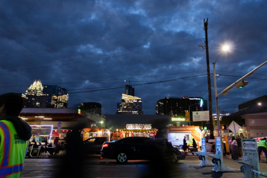 People walk past bars and food trucks on 6th street on March 14, 2023 as clouds form overhead.