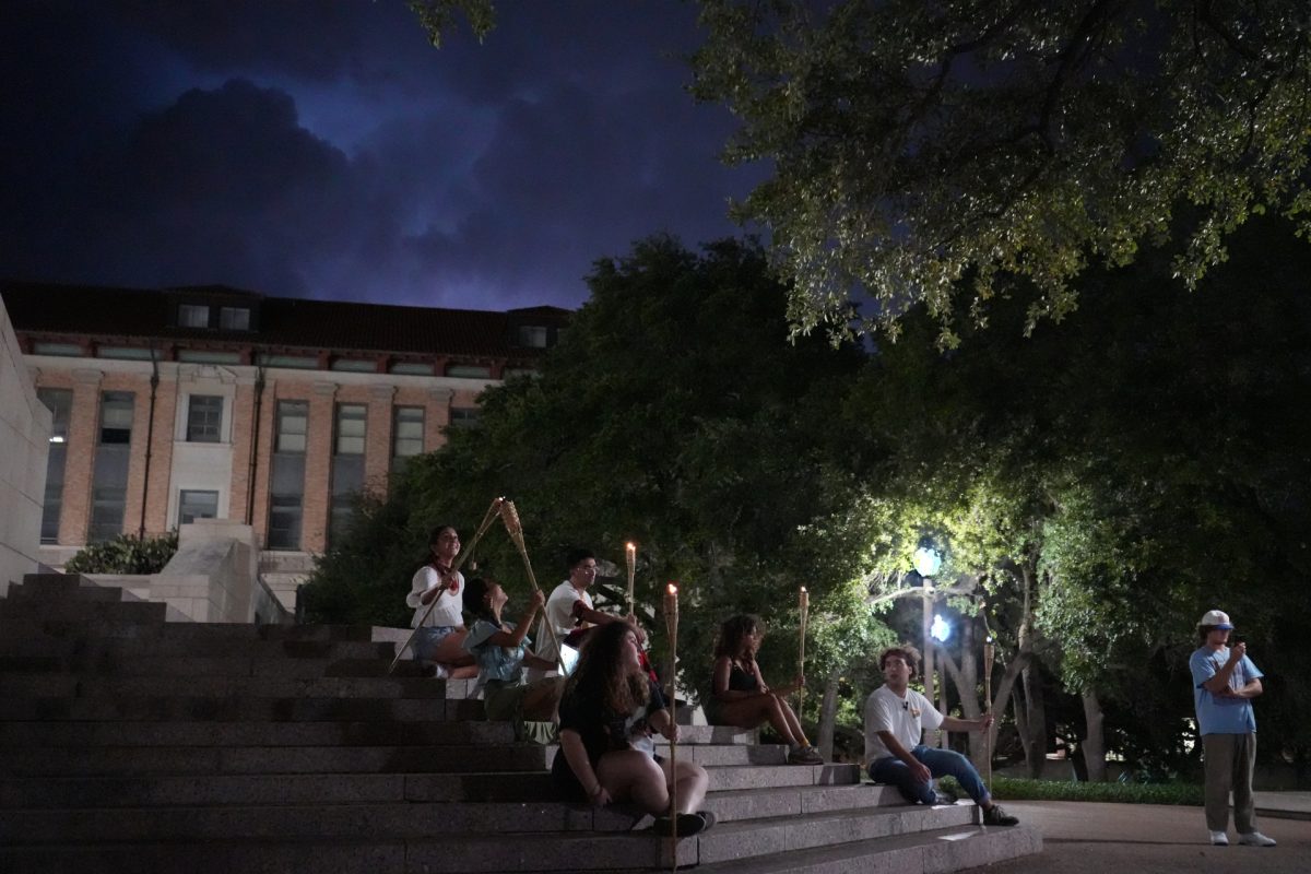 The Survivor Club players clutch their lit torches in the darkness beneath the UT tower on Sept. 24, 2023. They undergo individual interviews and cast their crucial votes to eliminate a fellow player while vigilantly guarding their torches from extinguishing.