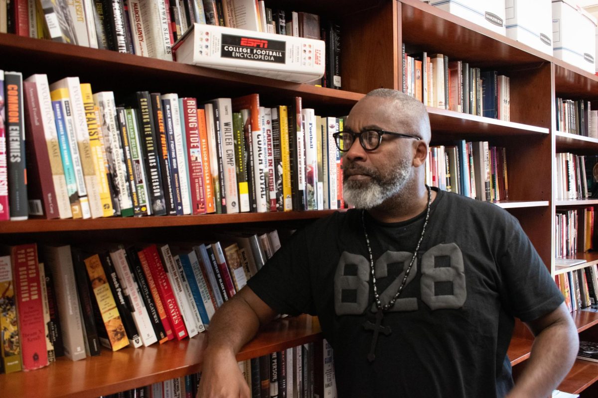 Dr. Leonard Moore, Founding Director of the College Football Research Project, poses next to a bookshelf in his office on Sept. 20, 2023. The shelves are almost entirely filled with football books including the ESPN College Football Encyclopedia.