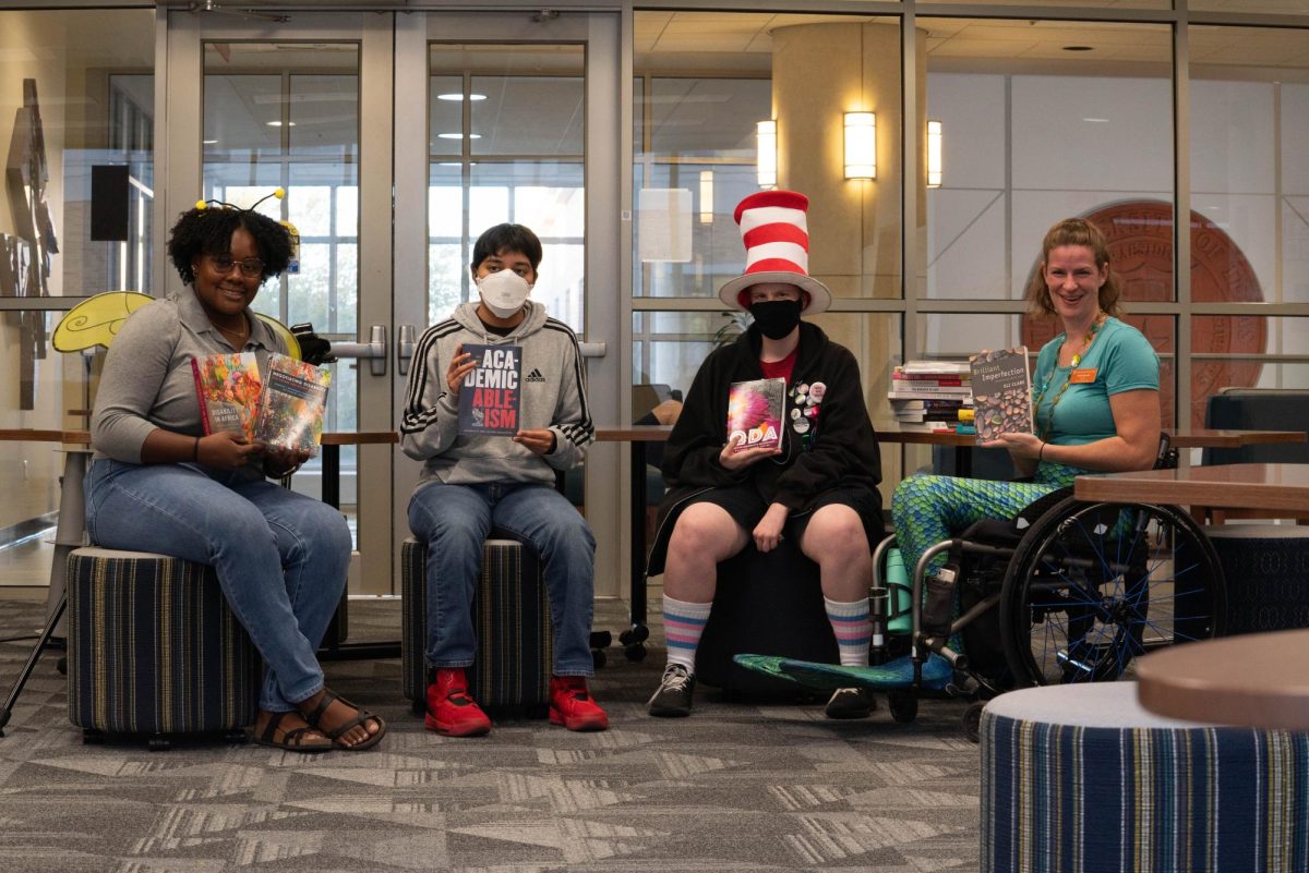 Jordan Jessie, Lira Amari Ramirez and Cat hold up books with Emily Shryock, the director of the DCC Library, at a DCC Halloween hangout on Oct. 17, 2023. The library is currently under renovation, but Shryock had many books from the library in her office. 
