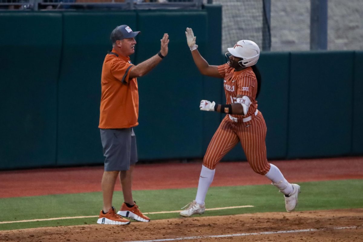 Freshman infielder Victoria Hunter high-fives head coach Mike White as she runs past third base after hitting a home run on Feb. 21, 2024 against Houston Christian University. Hunters home run allowed her fellow freshman Kayden Henry to score a point for the Longhorns.