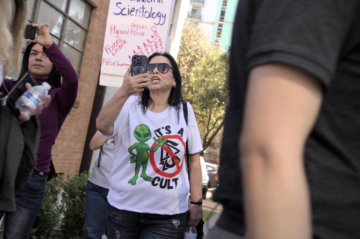 Protester Pearl Gomez records Scientology members leaving the opening ceremony on Saturday. Gomez, along with others present came from different cities in Texas and states to counterprotest the reopening of the Scientology Church building on Guadalupe Street.