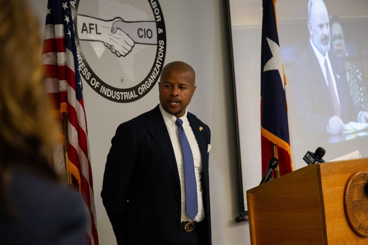 State Rep. Ron Reynolds, chair of the Texas Legislative Black Caucus, speaks at a press conference on Senate Bill 17 on Wednesday. Behind him plays a video of Rep. John Kuempel saying no staff would lose their jobs due to the bill; 66 UT employees were impacted by the Universitys SB 17 related layoffs, according to the Texas Conference of the AAUP.