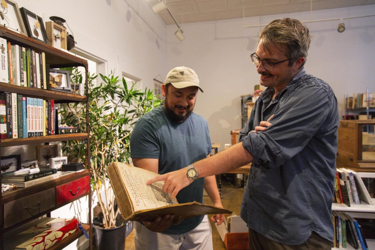 Owner Seth Gonzalez and employee Mark Lundy, a UT PhD student, read a book at Livra Books on Sept. 28, 2024. The book — the oldest in the store's collection — is from 1612.