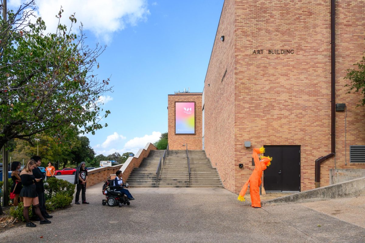 Bystanders waiting for the bus watch a student imitate an Air Dancer in performance at the College of Fine Arts Visual Arts Center on Tuesday, Oct. 29, 2024.