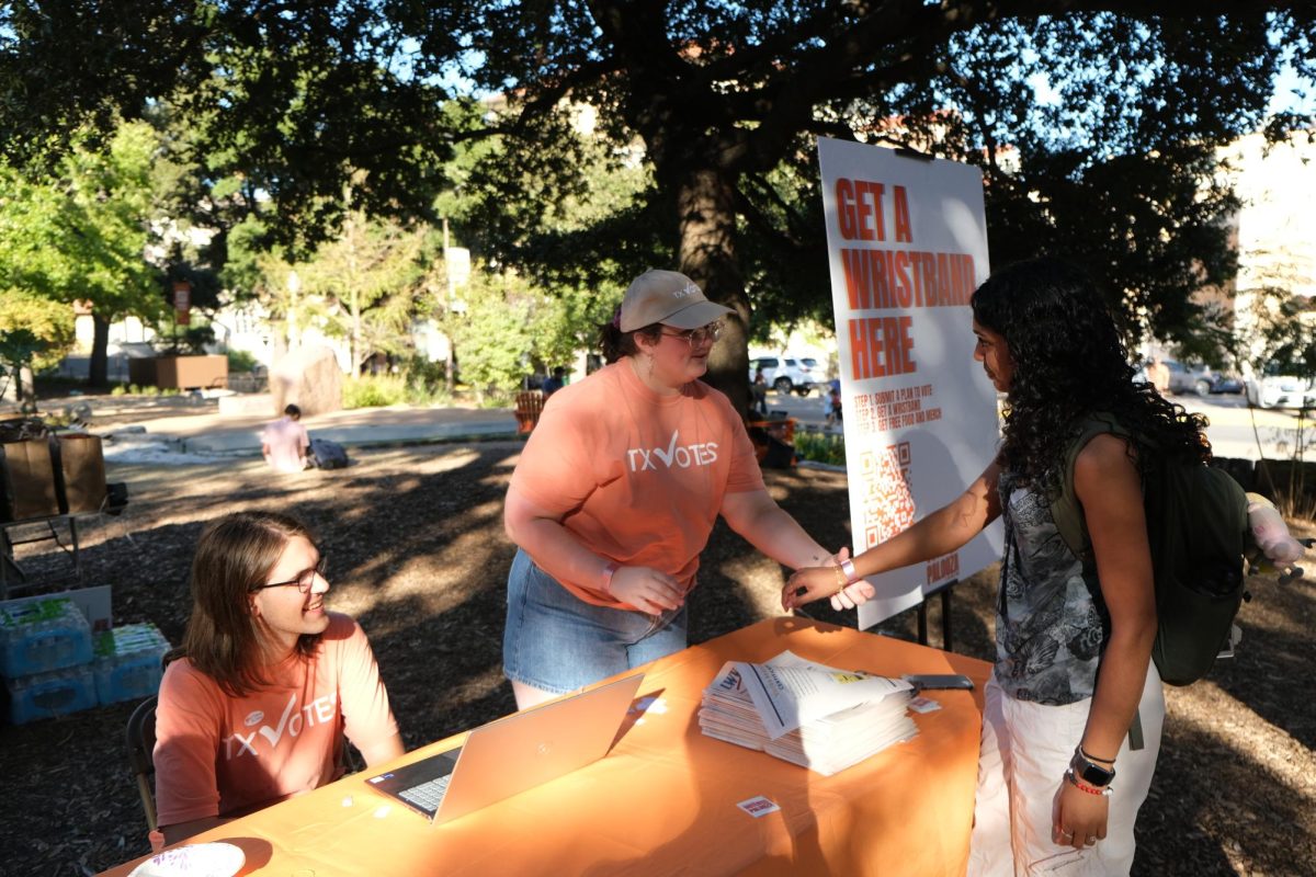 Government junior Guiliana Sodaro helps put a wristband on a UT student at Voterpalooza on Oct. 25, 2024.