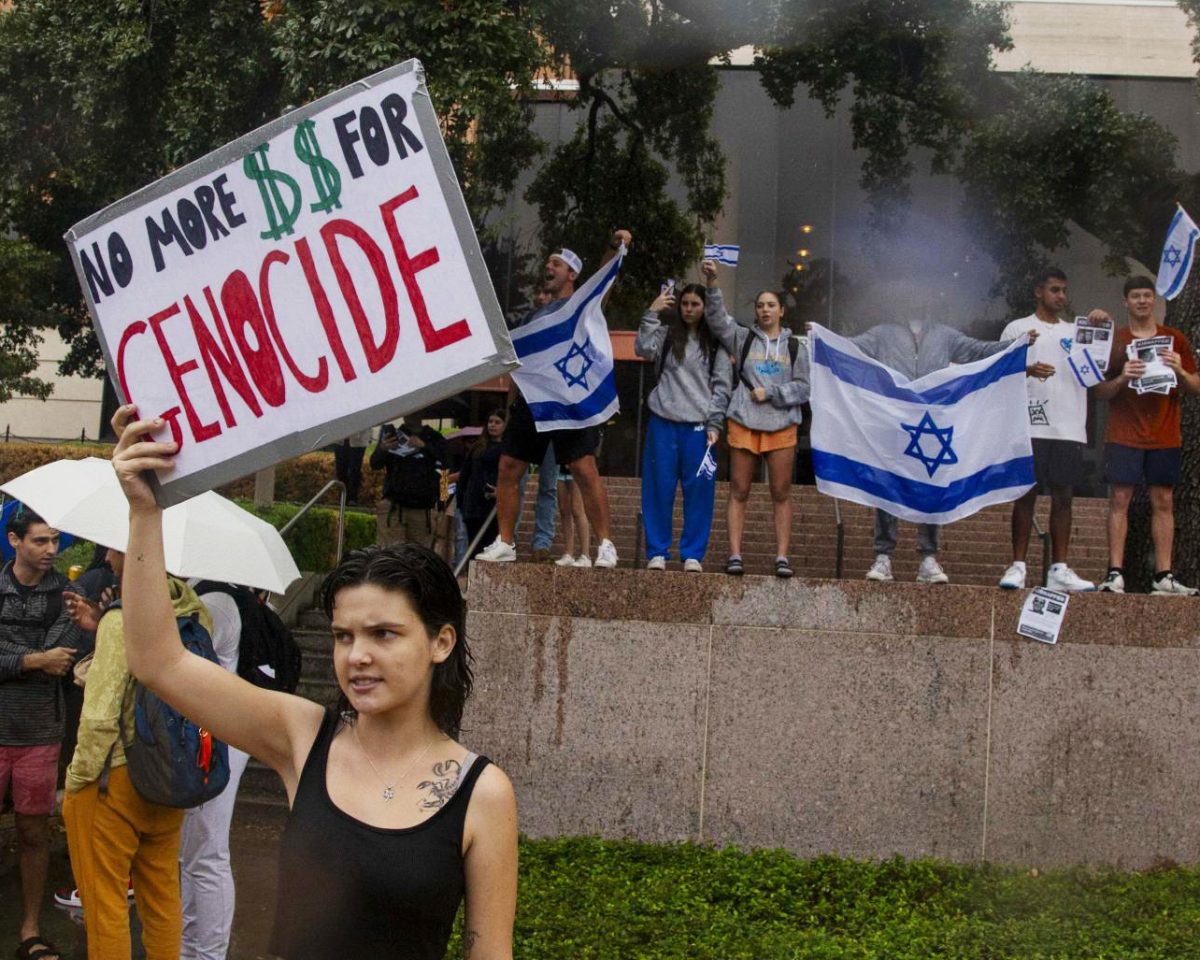 Pro-Israel counter-protestors wave Israel flags behind a pro-Palestine demonstrator holding a sign reading “No more $$ for genocide” on Nov. 9, 2023.