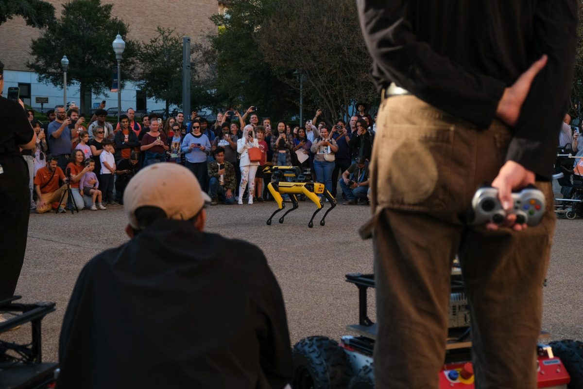 Individuals watch as B3V0, a Boston Dynamics quadruped robot with a mounted manipulator, dances to Beyonce's "TEXAS HOLD 'EM" at the UT Year of AI Robot Parade on Nov. 15, 2024