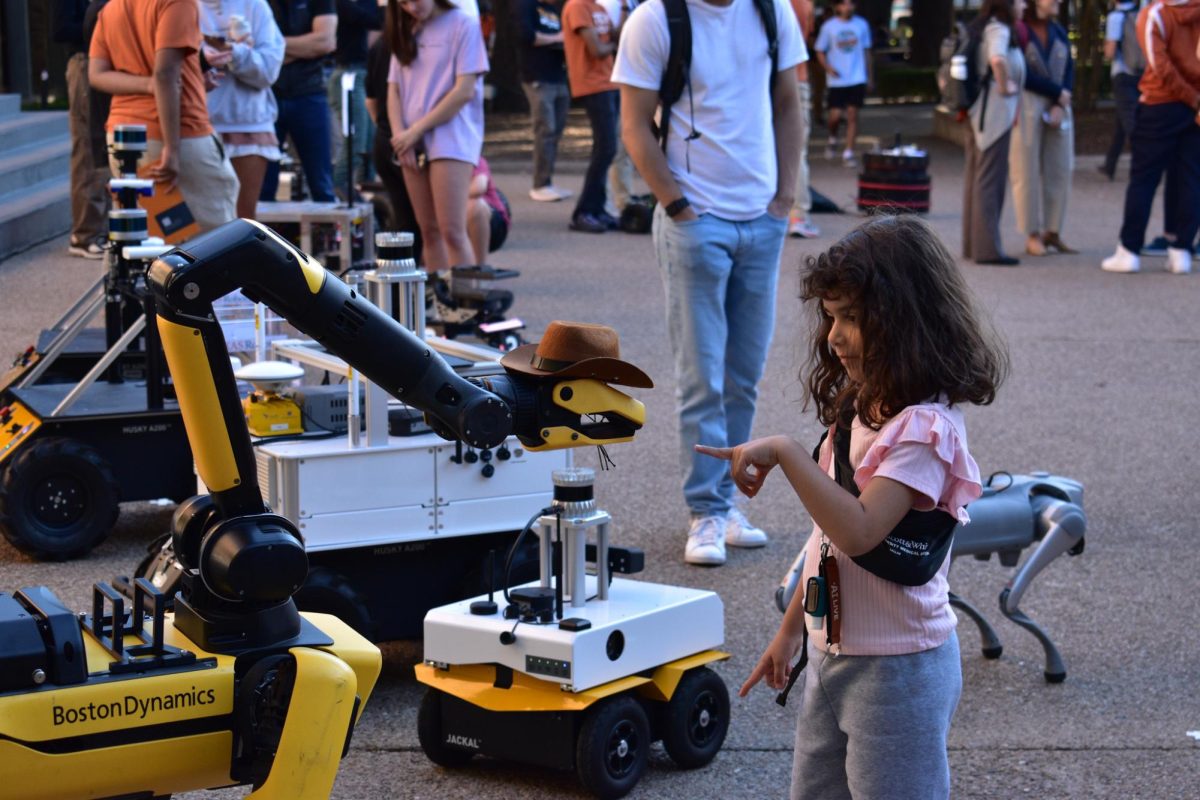 Sophie Koloft plays with Texas Robotics' B3VO, a Boston Dynamics quadruped robot with a mounted manipulator, at the UT Year of AI Robot Parade that happened on Speedway on Friday, November 15, 2024.