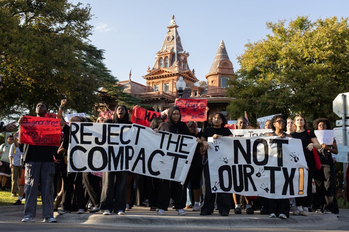 Protesters chant and hold up signs in front of the Littlefield House on Oct. 22, 2025.  The protest was organized by Not Our Texas in opposition to Trump’s compact.