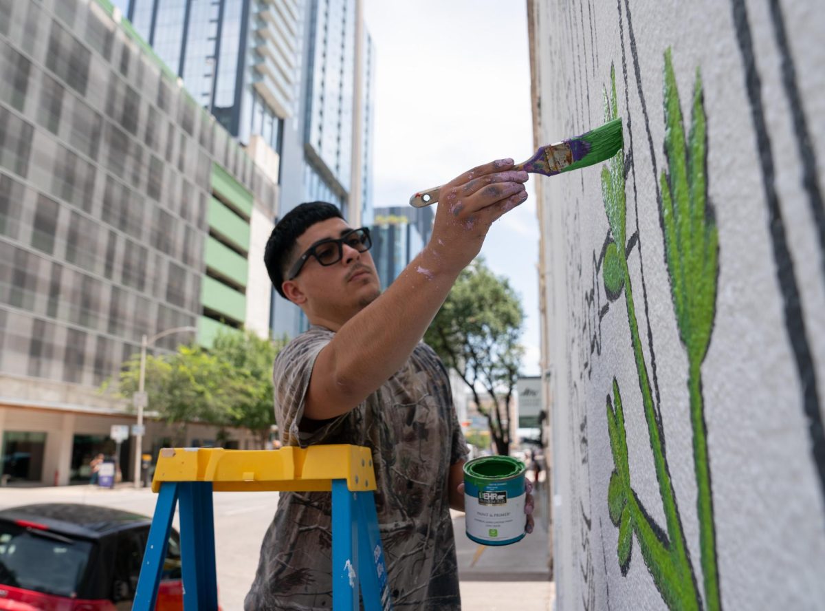 Bieke Campos reaches past his ladder with a brush covered in green paint to begin his first mural on Aug. 17. 