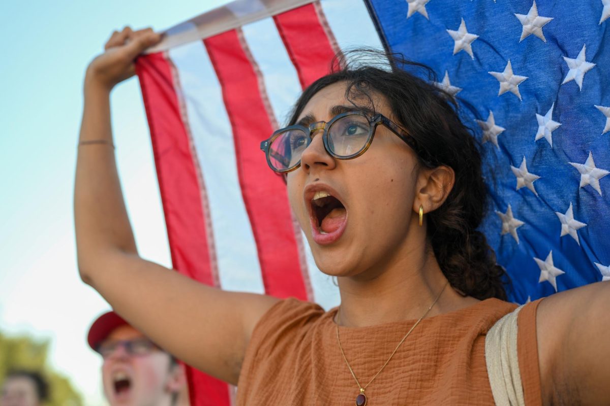 Waving the American flag over her head, humanities honors senior Ava Hosseini cries out in objection of the compact proposed by President Donald Trump during the protest organized by SDS on Oct. 20 in front of the Tower.