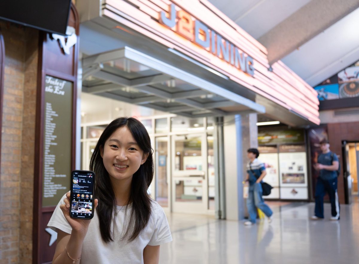 Finance junior Lisa Hadi poses with her phone displaying her Instagram account in front of J2 Dining on Thursday, Feb. 12. Hadi, known as The Foodie Patootie, is a social media food reviewer predominantly of the UT dining halls and food around Austin.