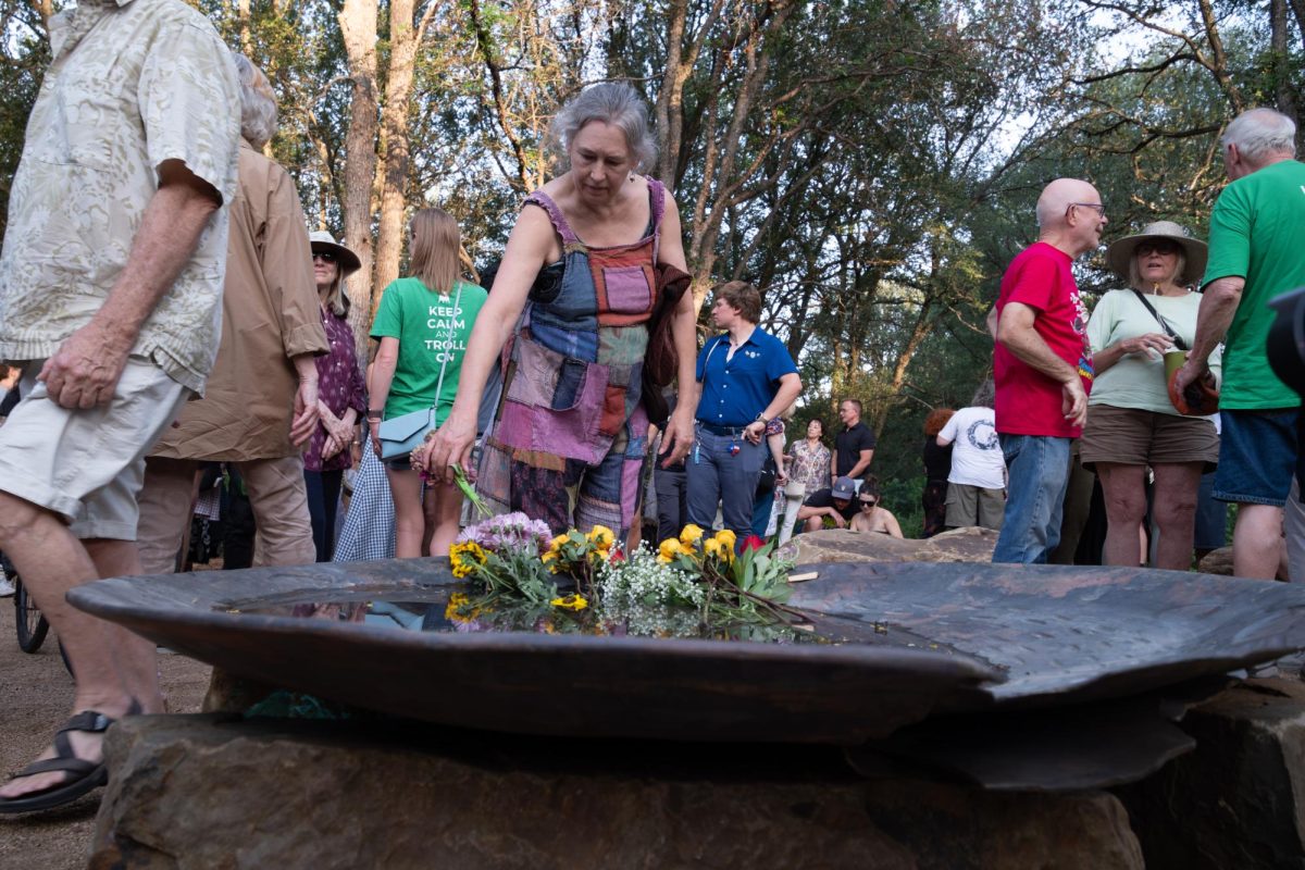 Charlotte Velasco places a flower in Malin's Fountain bowl during the "An Evening for Malin" memorial in Pease Park on Wednesday, June 24.